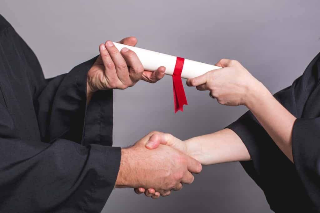 A graduate receiving a rolled certificate with a handshake