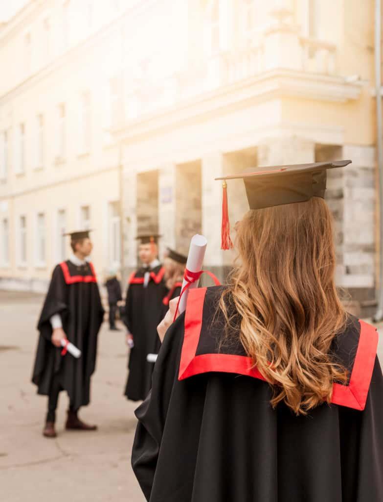 A graduate in cap and gown seen from behind outside a university building
